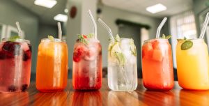 Assorted colorful agua frescas made with fresh fruit, citrus, and herbs, served over ice in glass jars.